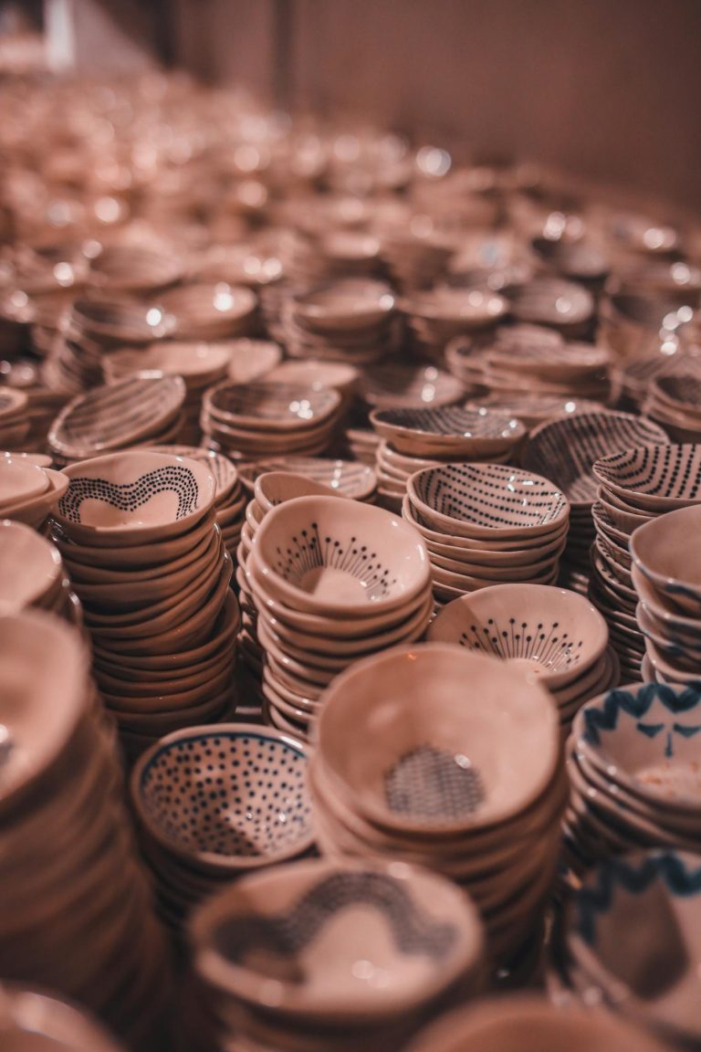 Rows of intricately designed handmade ceramic bowls stacked closely in soft lighting.